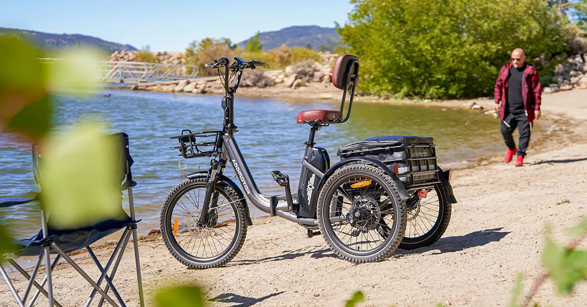 Addmotor electric trike parked on a sandy lakeside beach, featuring a sturdy rear cargo rack and comfortable padded seat, ideal for outdoor adventures.