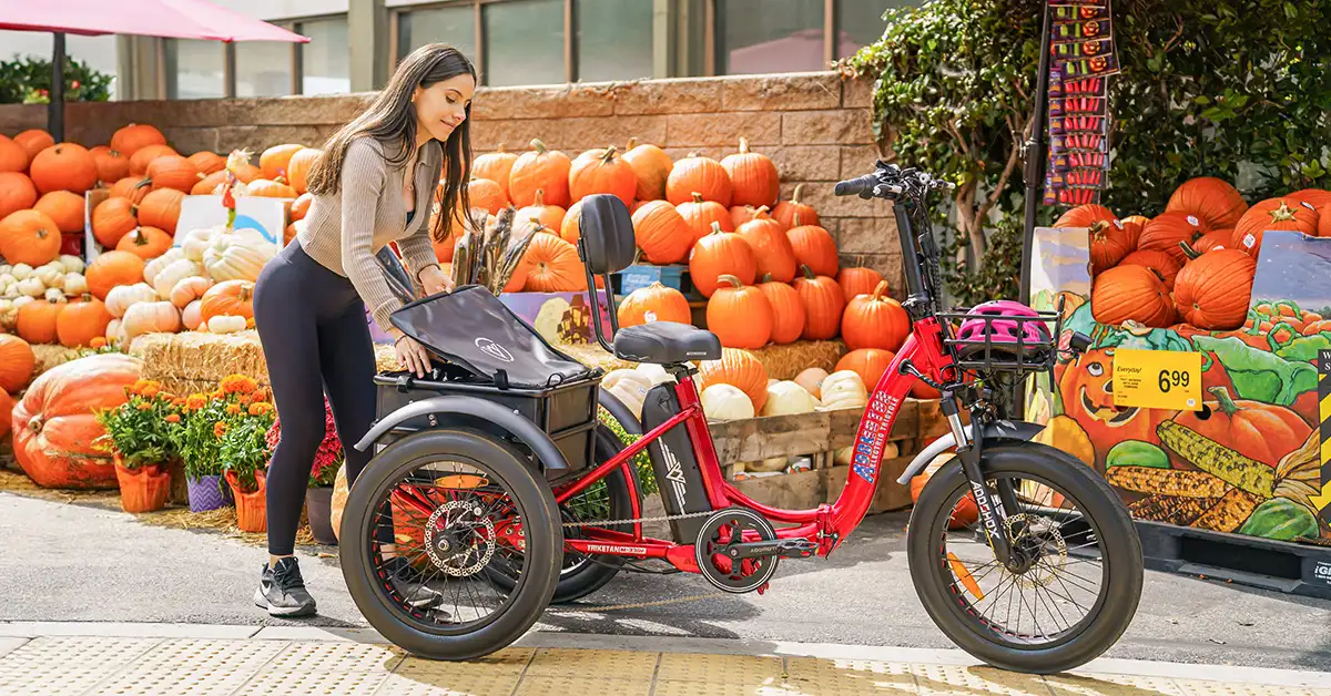 Triketan M-330F red electric trike parked near a vibrant outdoor produce stand, featuring a spacious rear cargo area filled with pumpkins.